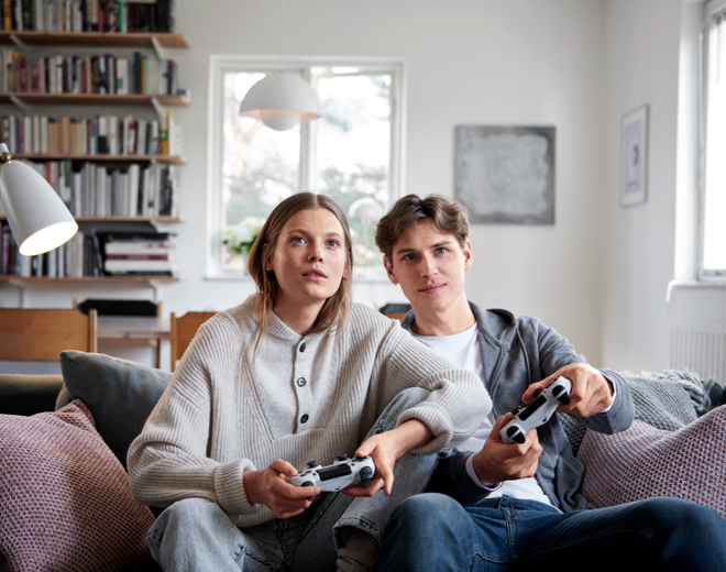 Två ungdomar som sitter i en soffa och spelar tv-spel