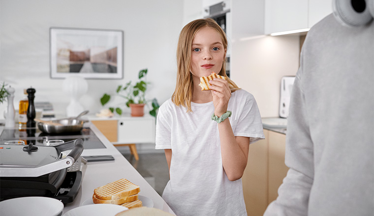 Flicka äter en macka i köket