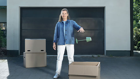 Kvinna som står framför ett garage och har massa flyttkartonger runt sig