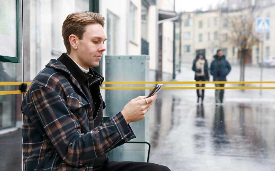 Man som sitter vid en busshållplats och tittar i sin mobiltelefon