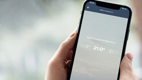 En hand håller i en mobiltelefon där man kan reglera värmen