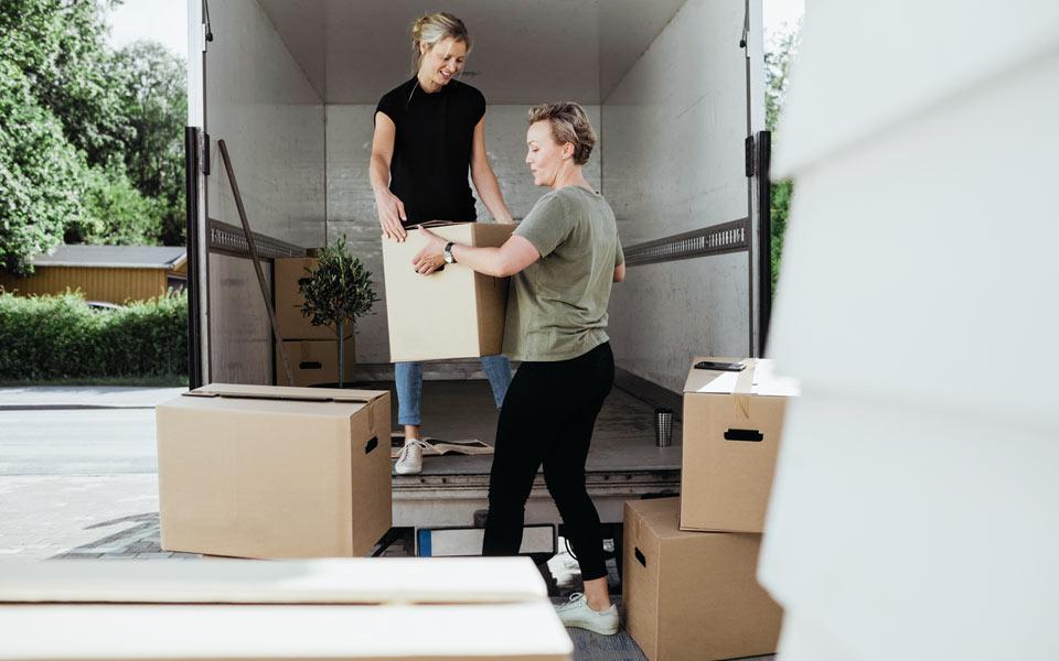 Två kvinnor som bär ut flyttkartonger från lastbil
