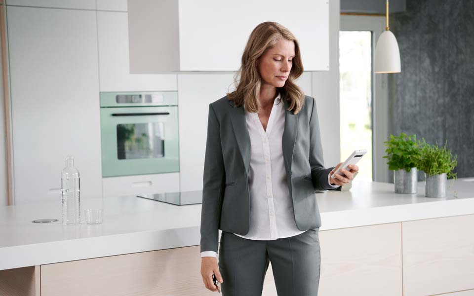 Kvinna som står i ett kök och tittar i en mobiltelefon