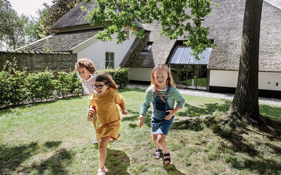 Tre barn som springer i en solig trädgård