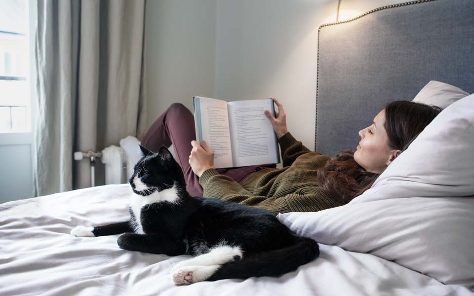 Kvinna som ligger i sängen och läser med en katt bredvid