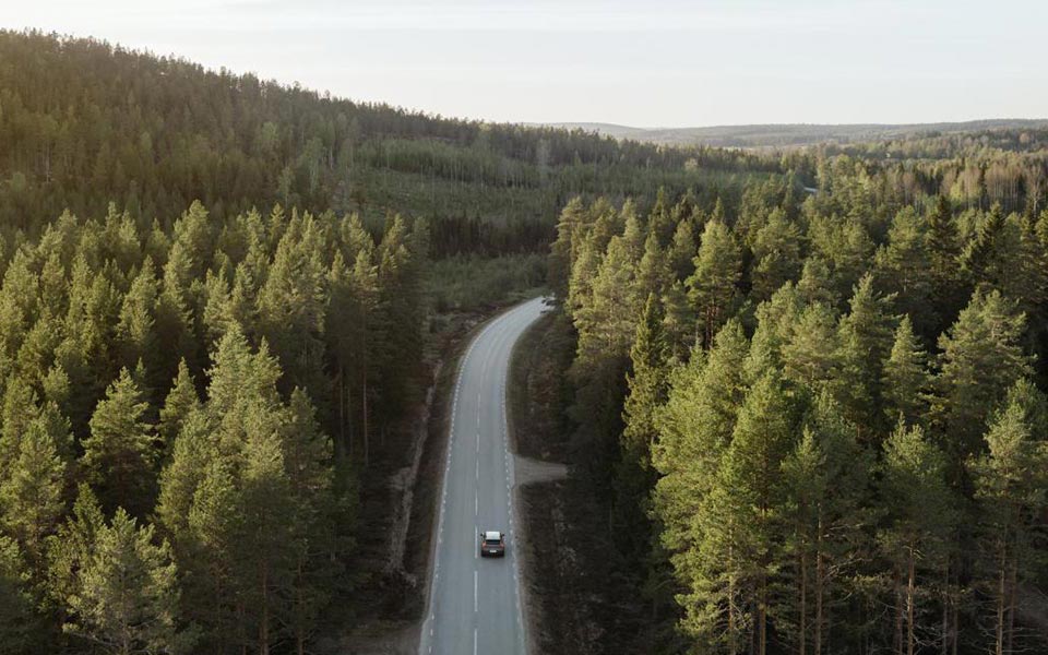 En bil kör på en väg genom tät grön skog, sedd uppifrån
