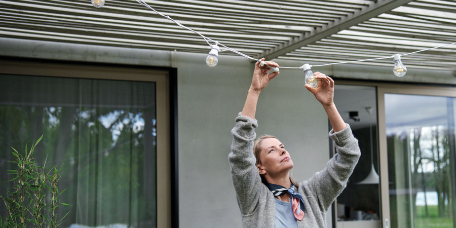 Kvinna som justerar en ljusslinga på en uteplats