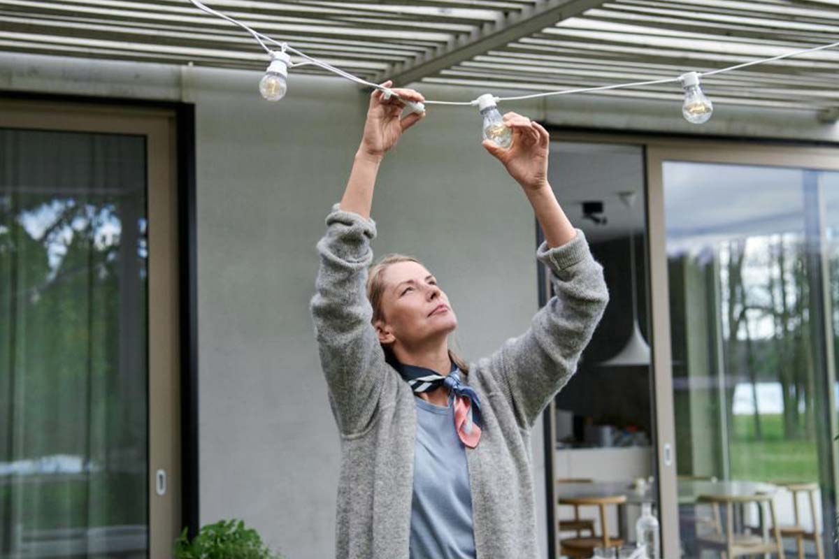 Kvinna som justerar en ljusslinga på en uteplats