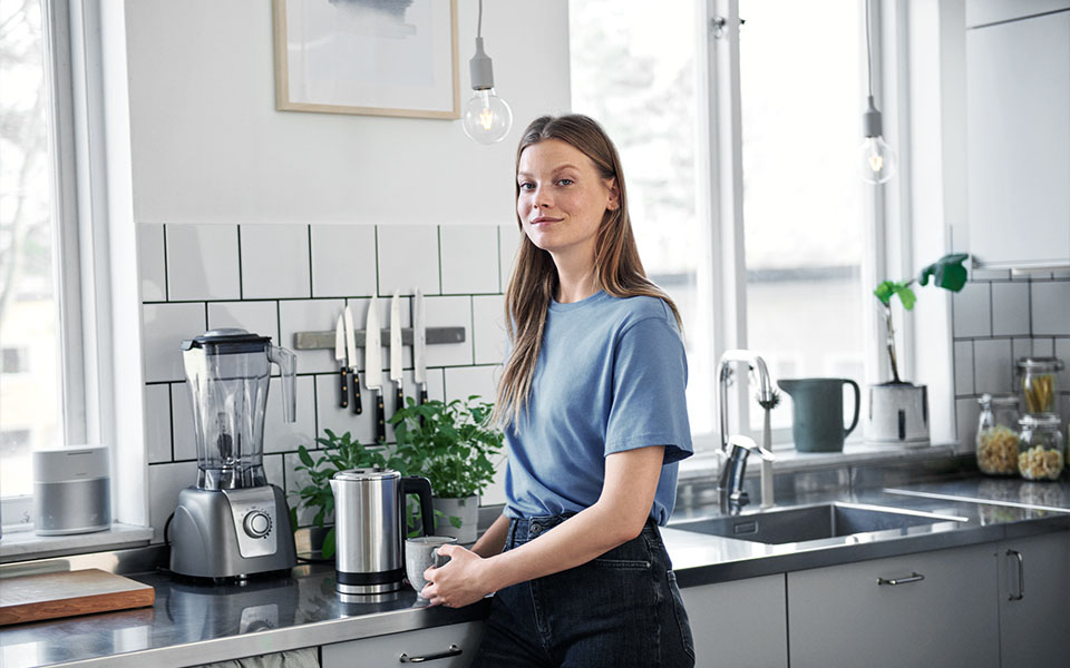 Kvinna som står i ett kök och håller en kopp kaffe i handen