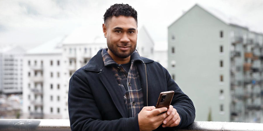 Man som står framför flerbostadshus och håller i en mobiltelefon.
