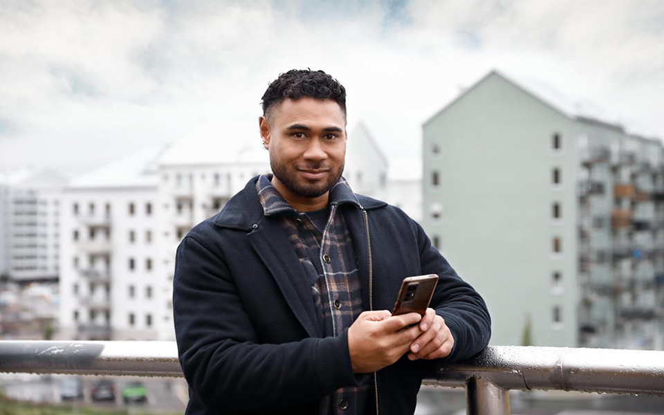 Man som står framför flerbostadshus och håller i en mobiltelefon.