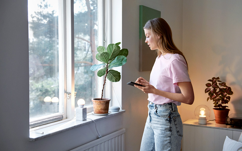 Ung kvinna som står vid ett fönster och håller i en mobiltelefon
