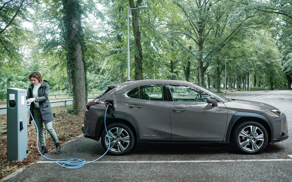 En kvinna som laddar en grå elbil på en parkeringsplats