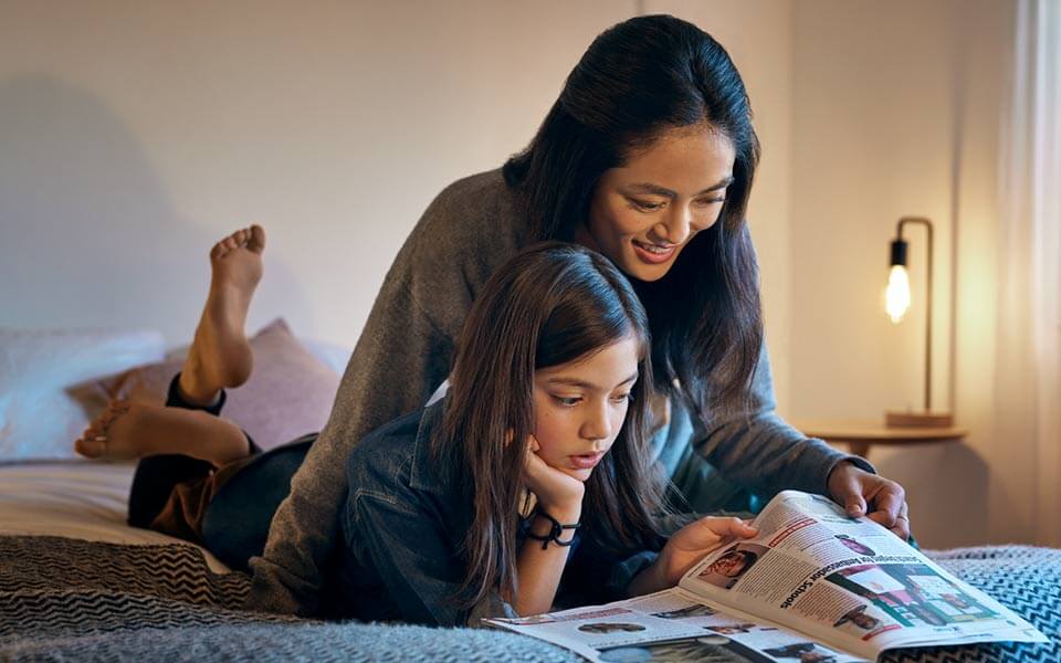 Mamma och dotter ligger i sängen och läser en tidning