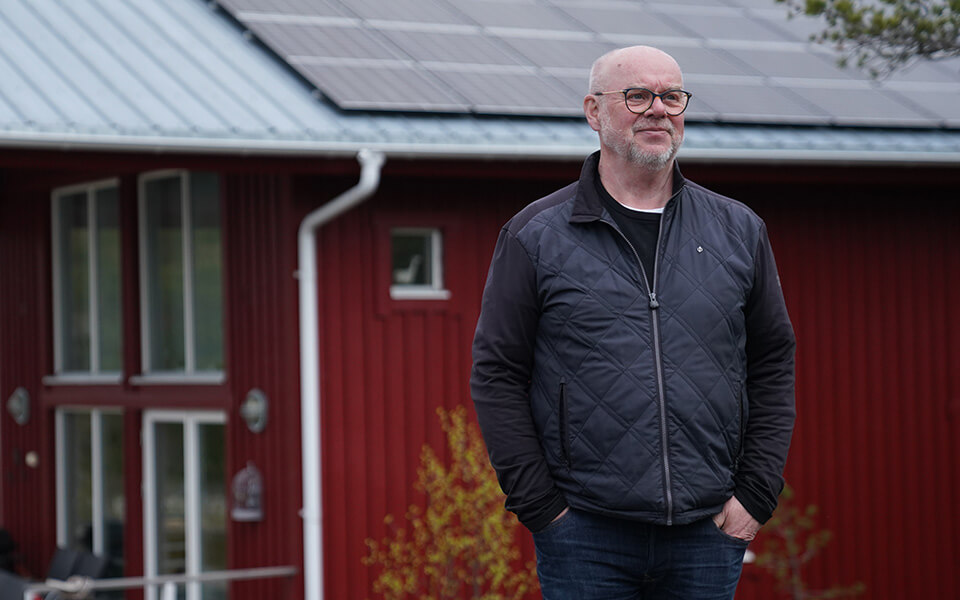 Ulf Berggren står framför sin sommarstuga med solpaneler på taket