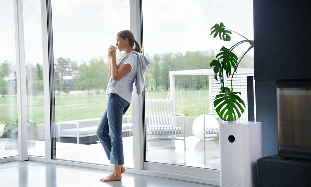 Kvinna håller i en kopp lutandes mot glasväggar i modern villainteriör