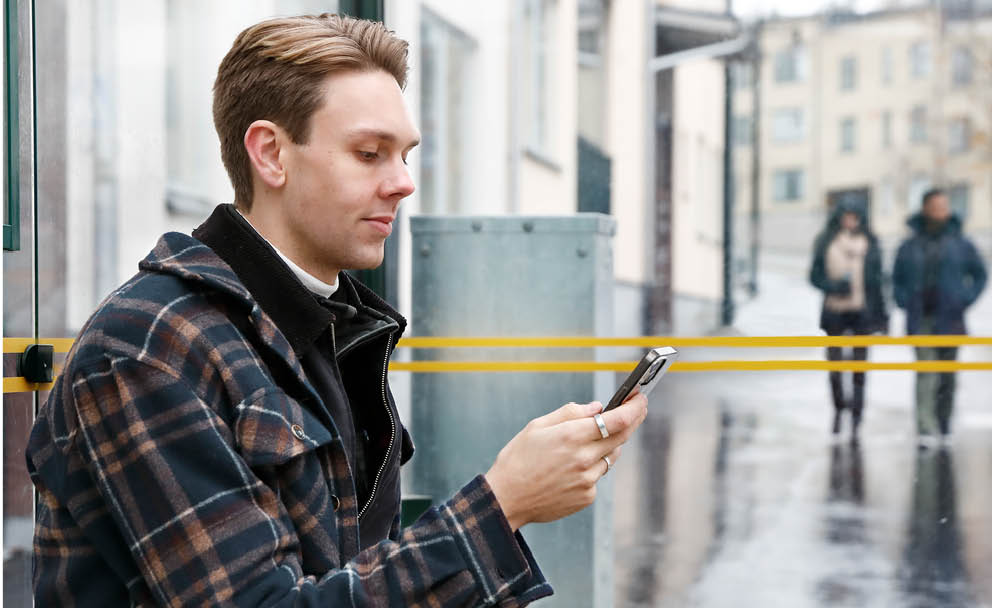 Man sitter vid busskur och skrolla på telefonen.