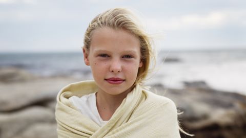 Närbild på flicka som står invirad i en handduk med svenska kusten bakom sig