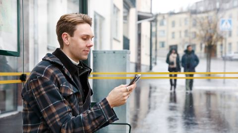 Man som väntar på bussen i en busskur och scrollar på mobilen
