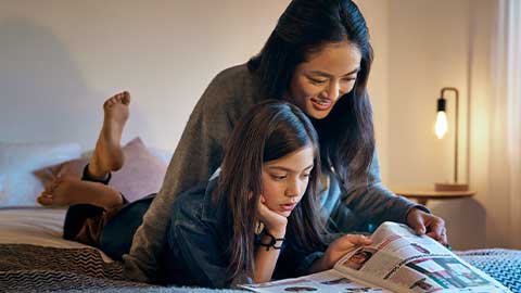Kvinna och barn ligger i en säng och läser en tidning tillsammans