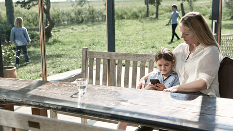 Äiti ja lapsi istuvat ulkona katsomassa älypuhelinta