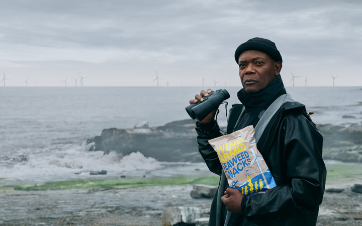 Man som står framför vindkraftverk och håller en chipspåse i famnen