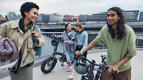 Fyra personer går med sina elcyklar över en bro.