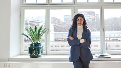 Kvinna på ett kontor som står vid ett fönster med armarna i kors