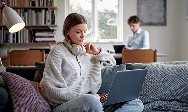 Kvinna som sitter i soffa och tittar ned i sin bärbara dator