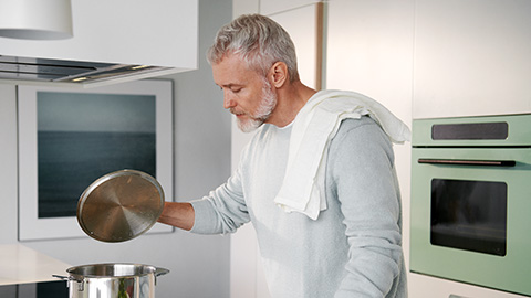 En äldre man lagar mat vid spisen i ett kök