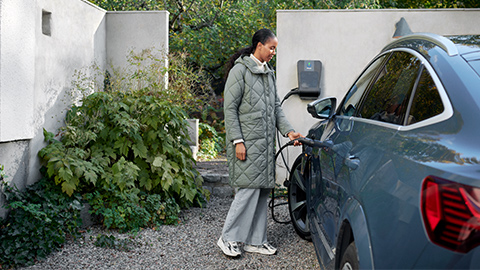 En kvinna som laddar elbilen på uppfarten