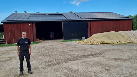 En man står utanför en lada med solceller på taket.