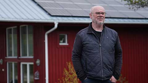Man står framför en röd sommarstuga med solpaneler på taket