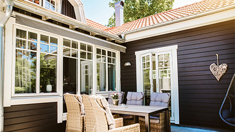 Uteplats vid ett brunt hus med vita fönster.