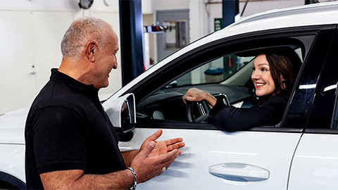 Kvinna sitter i en bil och får hjälp med besiktning av en man.